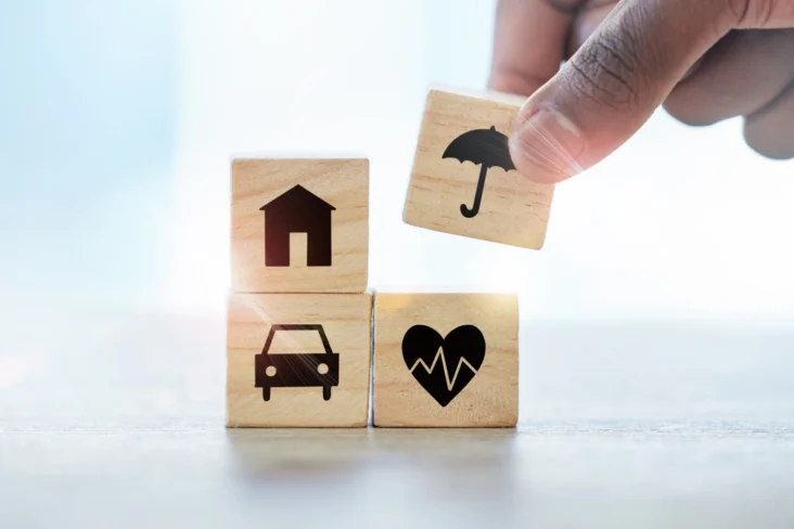 Imagem onde uma mão monta uma torre de blocos de madeira com pictogramas que representam vários seguros