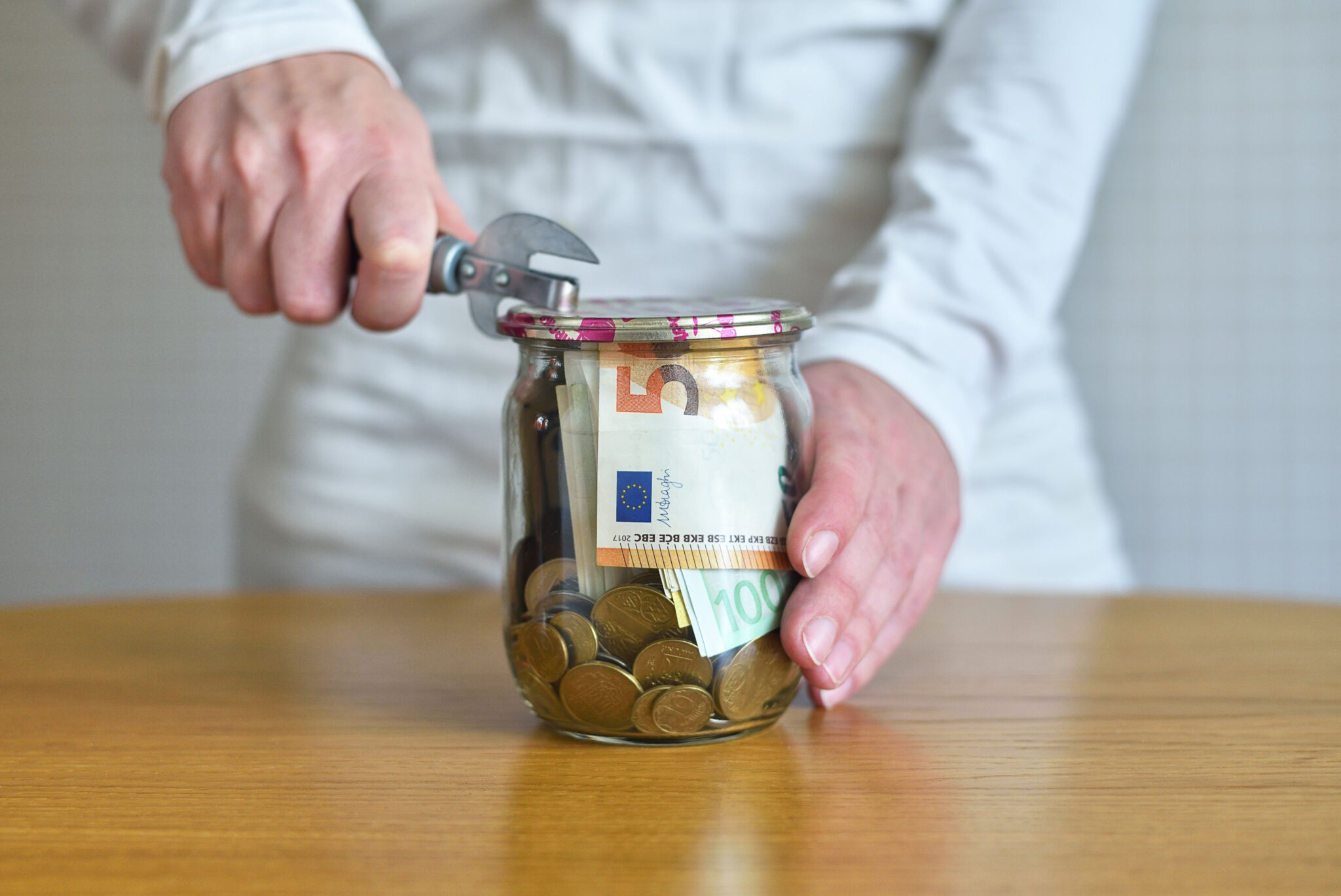 Transforme impulsos de consumo em oportunidades para poupar imagem de uma pessoa a tentar abrir um frasco com notas e moedas - para ilustrar artigo sobre Como transformar impulsos de consumo em oportunidades para poupar