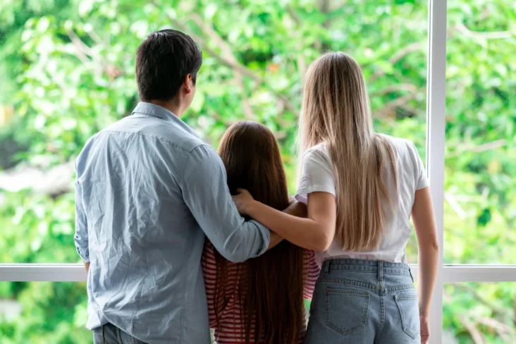 Imagem onde uma família olha com esperança para o futuro através da janela de casa