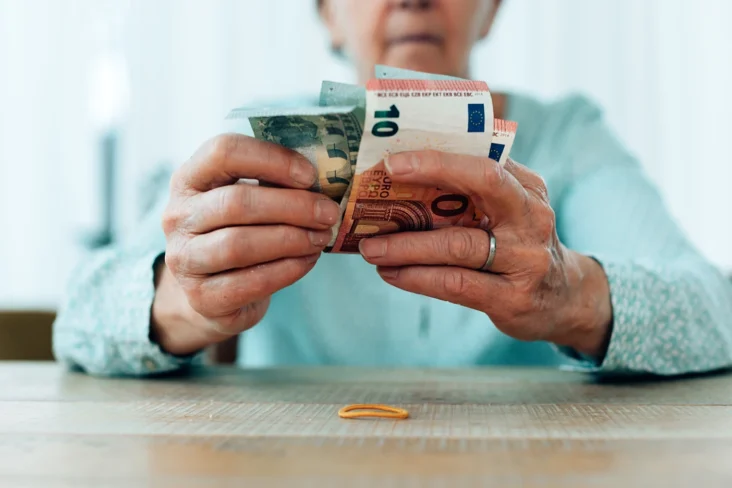 Imagem de uma mulher, idosa, a segurar em várias notas de euros