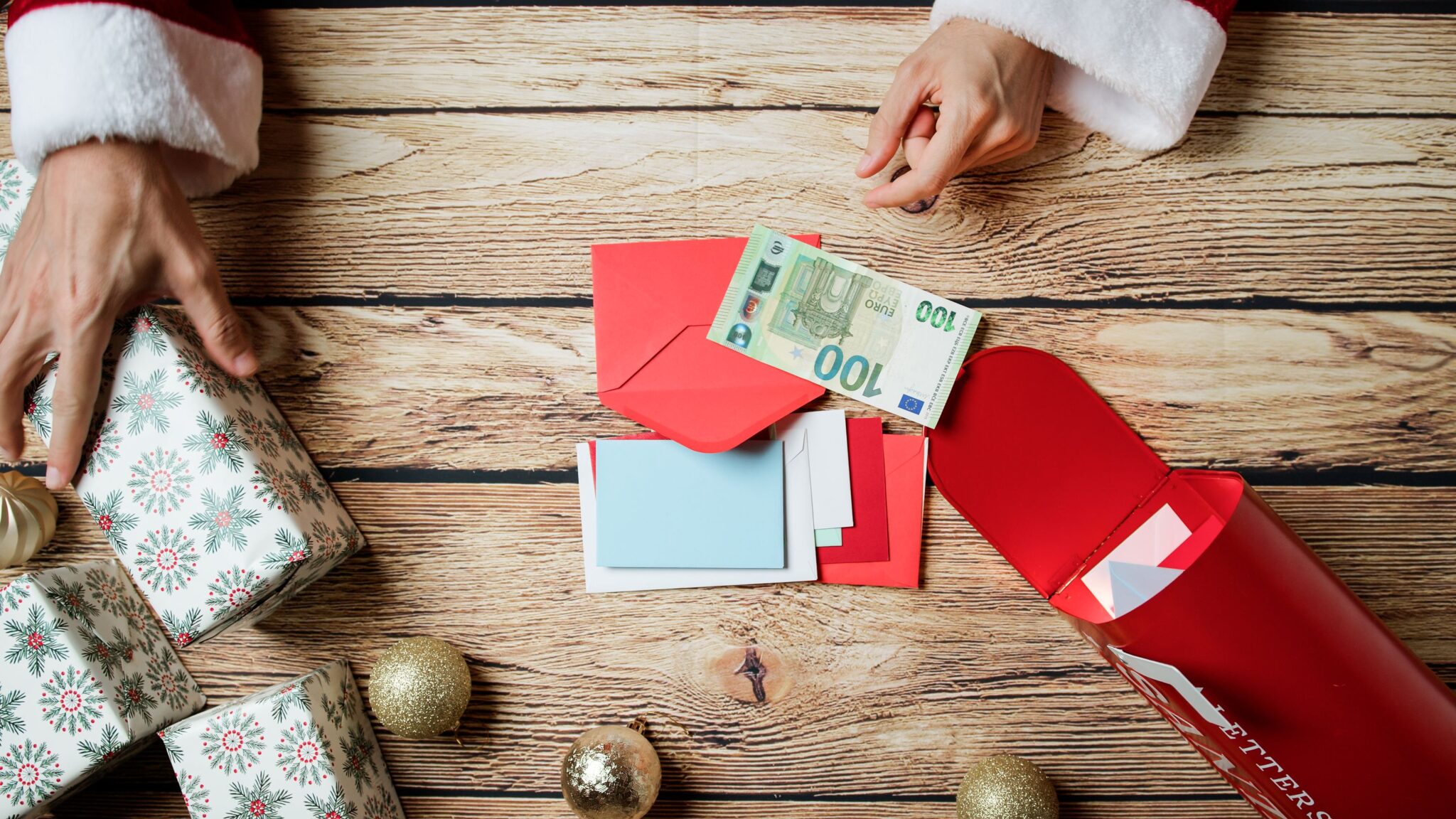 imagem de umas mãos do pai natal a mexer em embrulhos e envelopes com dinheiro - para ilustrar artigo sobre Subsídio de Natal: 5 erros que podem custar caro