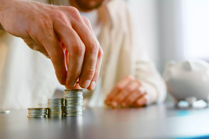 homem a empilhar moedas ao lado de mealheiro