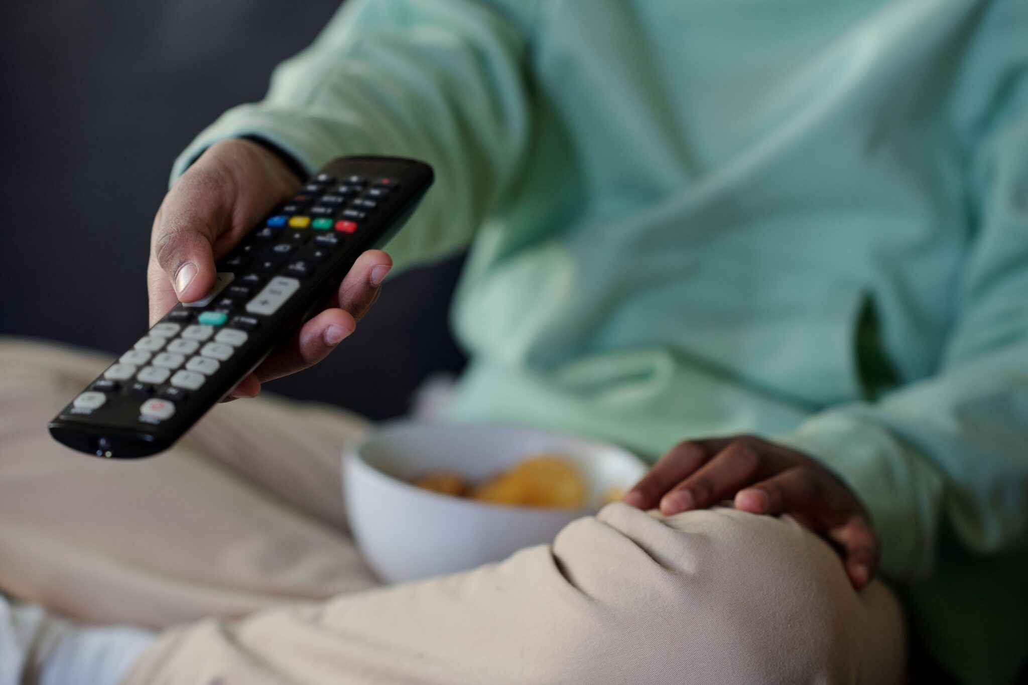 Janeiro é o melhor mês para mudar de operadora? pessoa sentada no sofá a usar um comando de televisão - para ilustrar artigo sobre Janeiro é o melhor mês para mudar de operadora? O que deve analisar