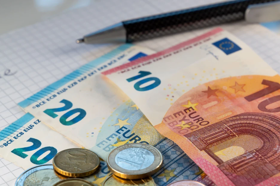 Imagem decorativa de notas e moedas sobre uma folha de cálculo e caneta