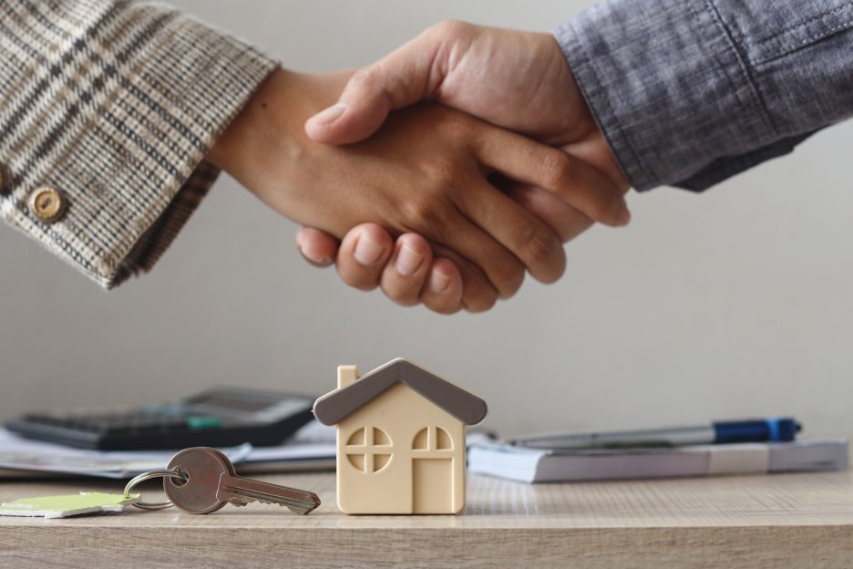 Duas pessoas a apertar as mãos, em cima de casa em miniatura