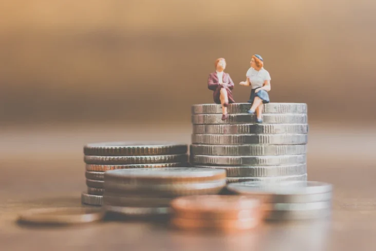 Imagem de um casal de bonecos sentados em moedas