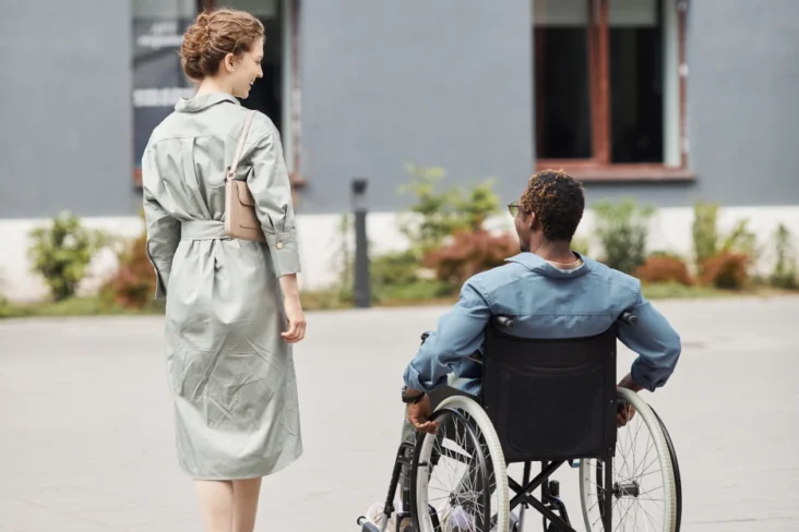 Imagem onde uma mulher acompanha um homem com necessidades físicas numa cadeira de rodas