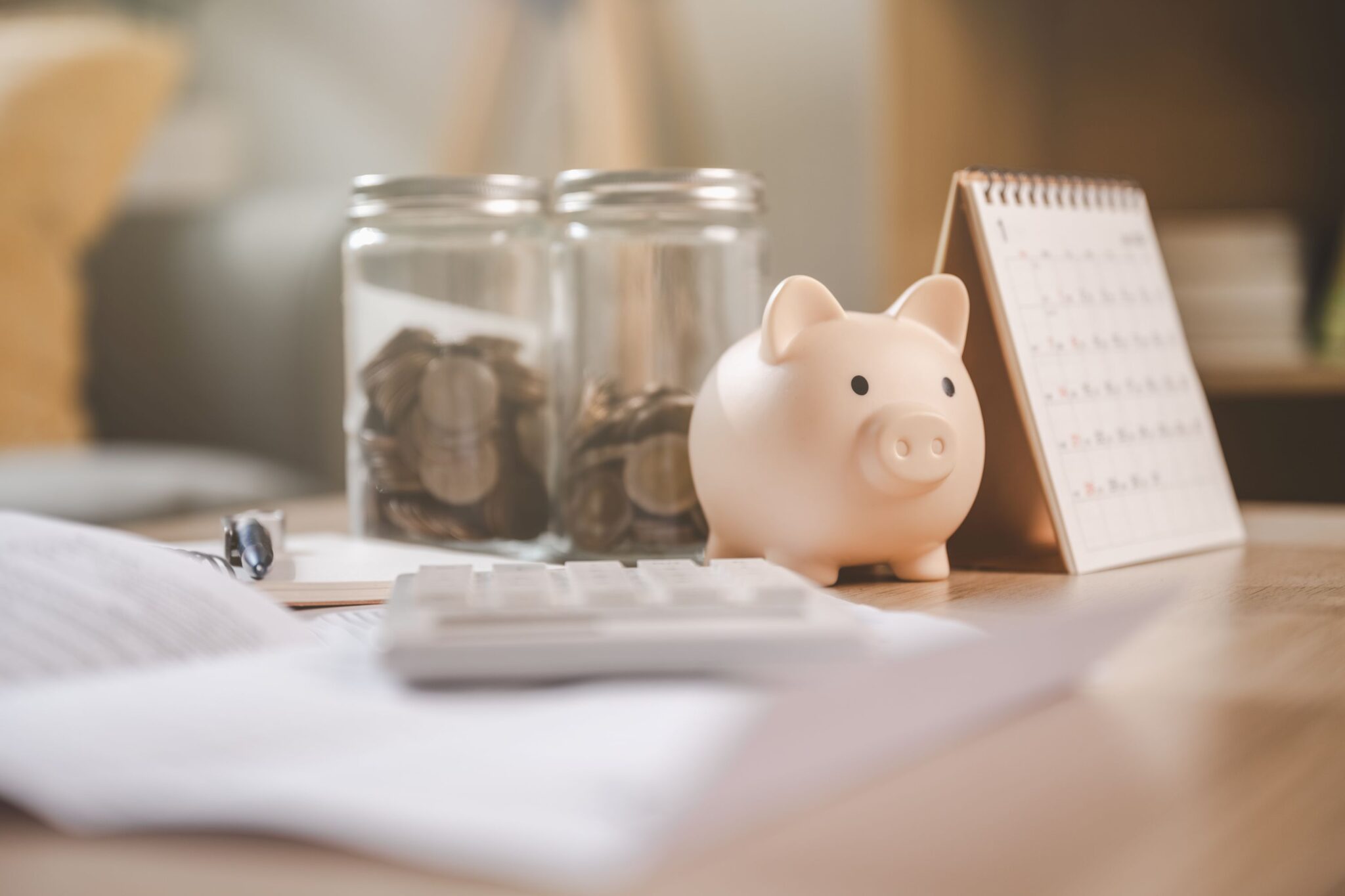 imagem de dois potes com moedas, uma calculadora, um mealheiro e um calendário em cima da uma mesa - para ilustrar artigo sobre erros financeiros típicos do início do ano