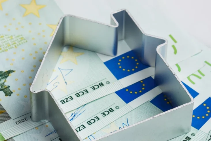 Imagem de uma forma de casa sobre notas de euro, simbolicamente representando a ajuda ao pagamento da habitação