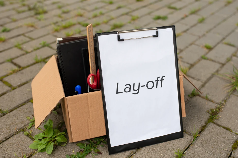 Imagem de uma resma de papel com a palavra Lay-off e material de escritório dentro de uma caixa de cartão