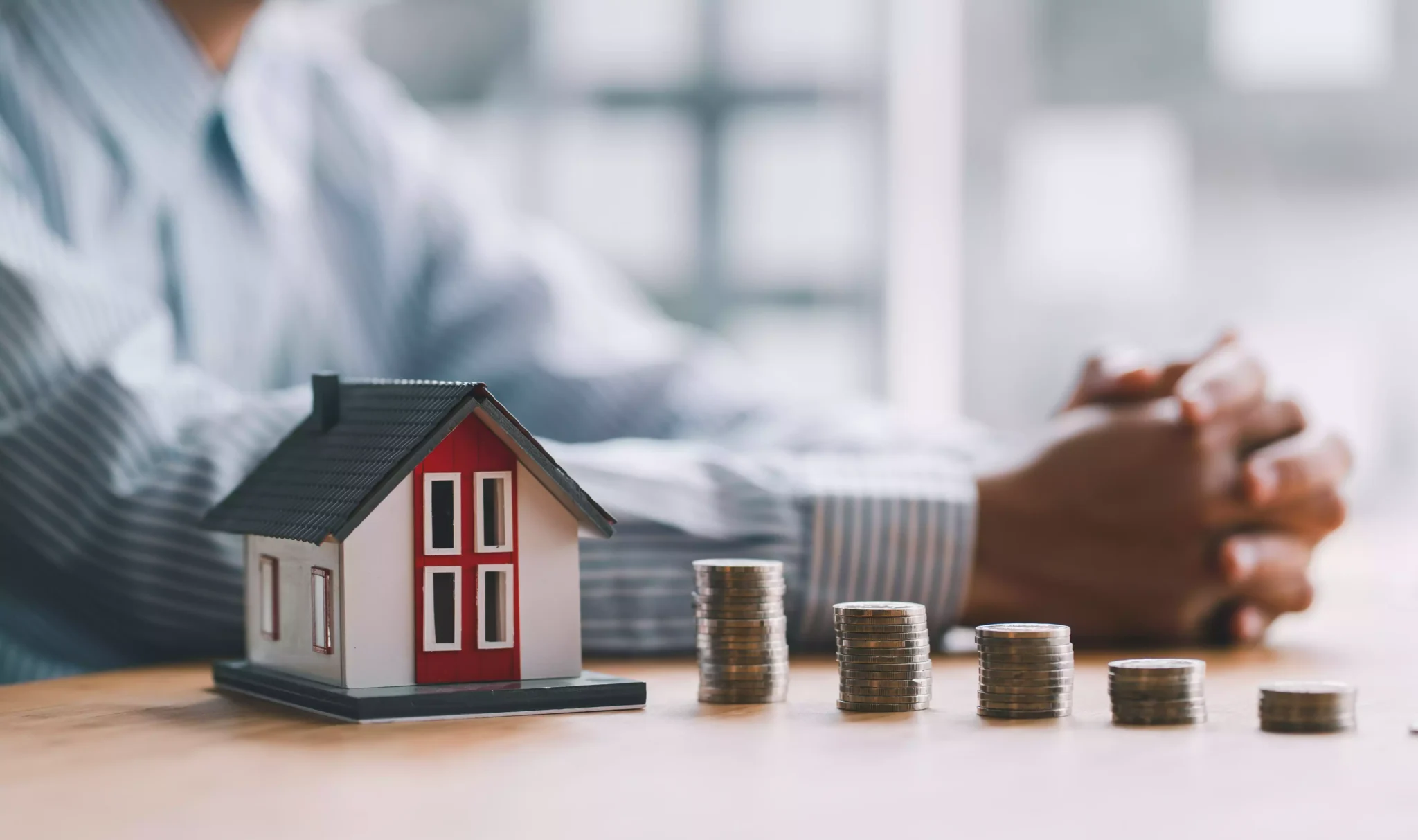 Homem junto a miniatura de casa e pilhas de moedas