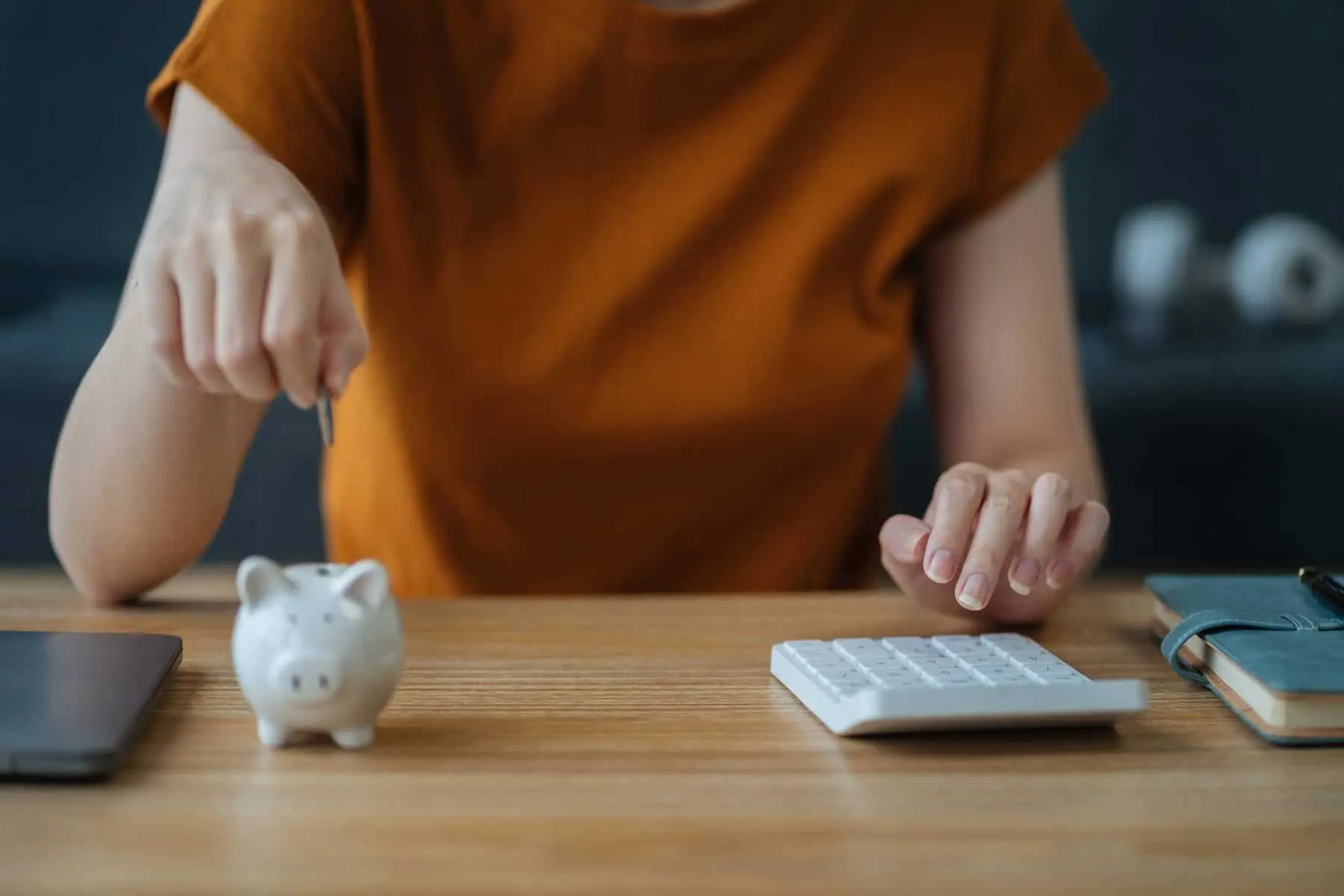 mulher a colocar moedas num porquinho mealheiro e com calculadora na outra mão