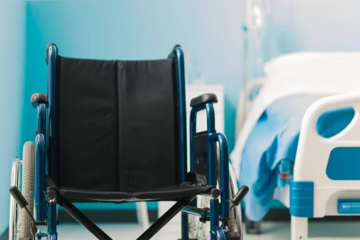 Imagem de uma cadeira de rodas num quarto de hospital, representativo de cuidados de saúde