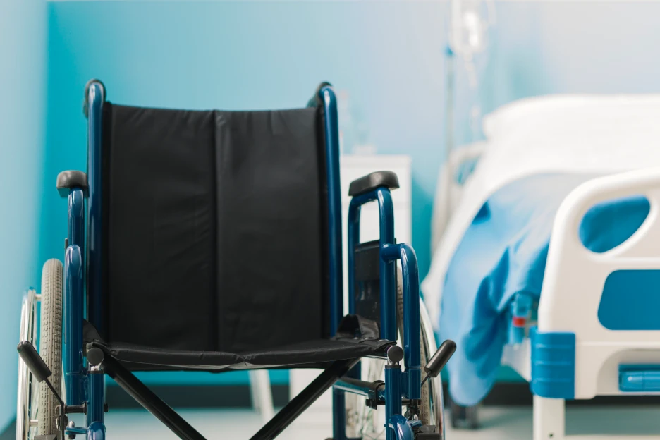 Imagem de uma cadeira de rodas num quarto de hospital, representativo de cuidados de saúde