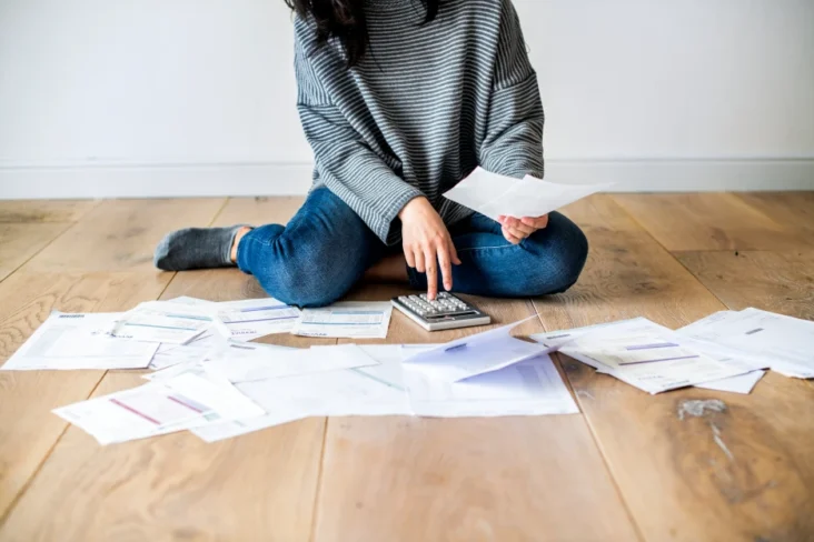 Imagem de uma mulher sentada no chão com várias folhas de dívidas às finanças
