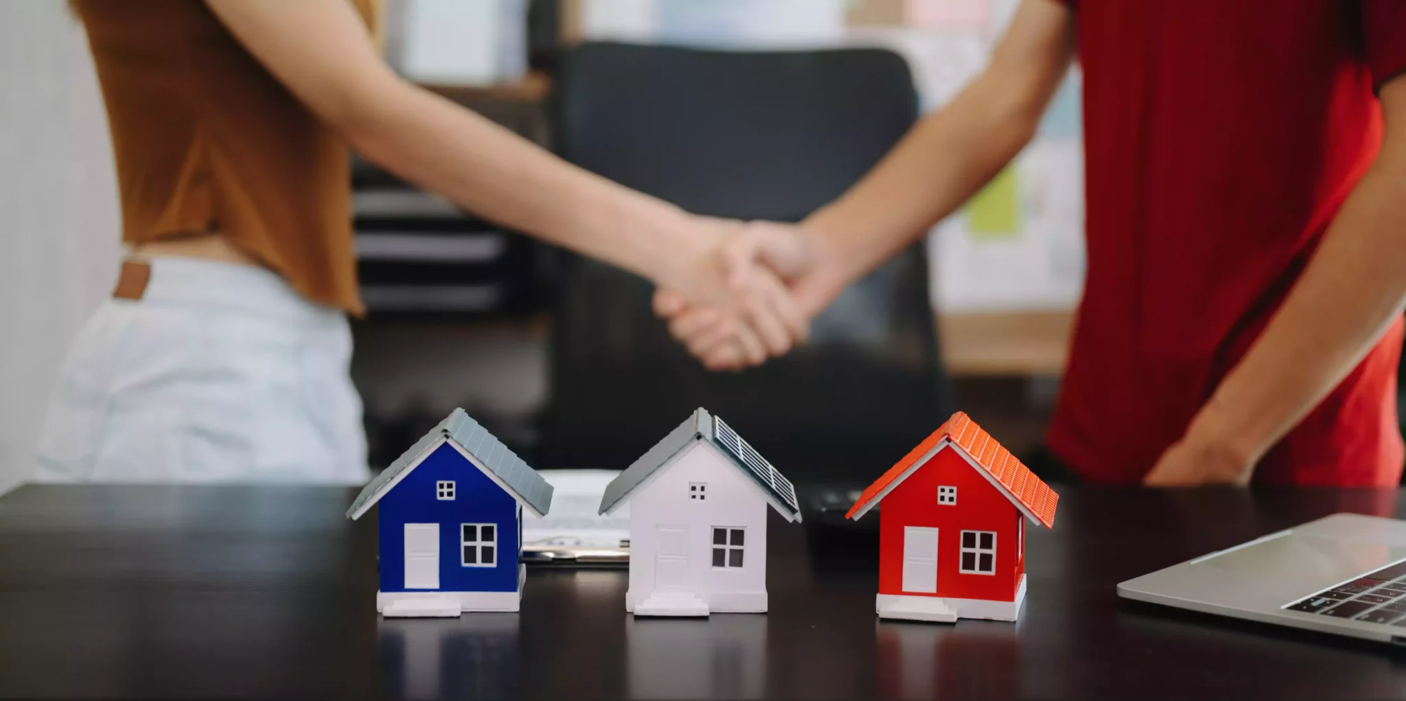 Peso da taxa variável no crédito habitação nunca foi tão baixo Duas pessoas a apertar a mão junto a maquetes de casas