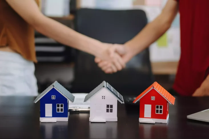 Duas pessoas a apertar a mão junto a maquetes de casas