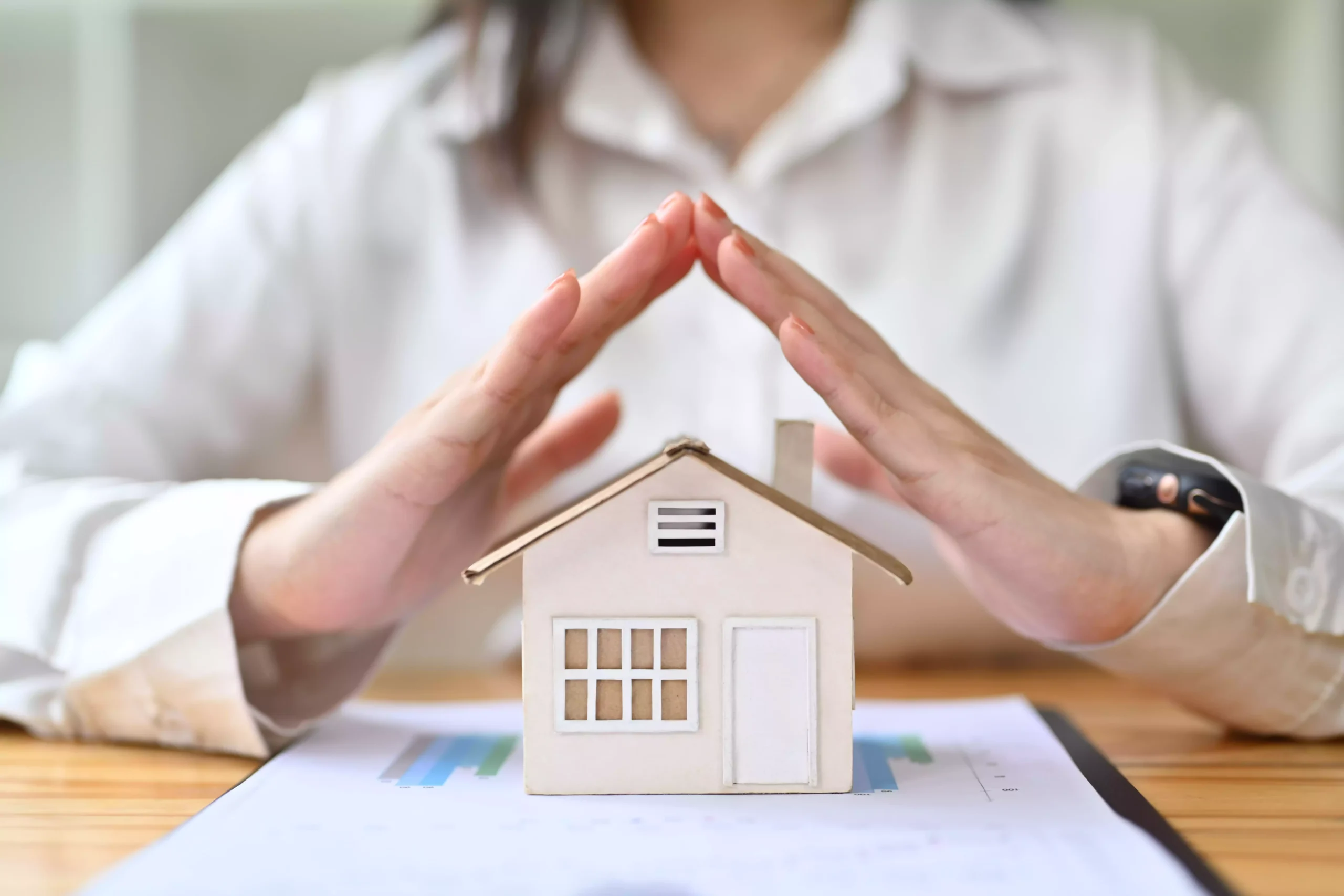 Mulher a proteger casa em miniatura com as mãos