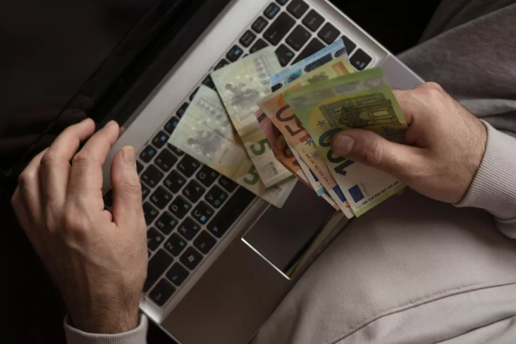 Homem a usar computador com notas de euro na mão